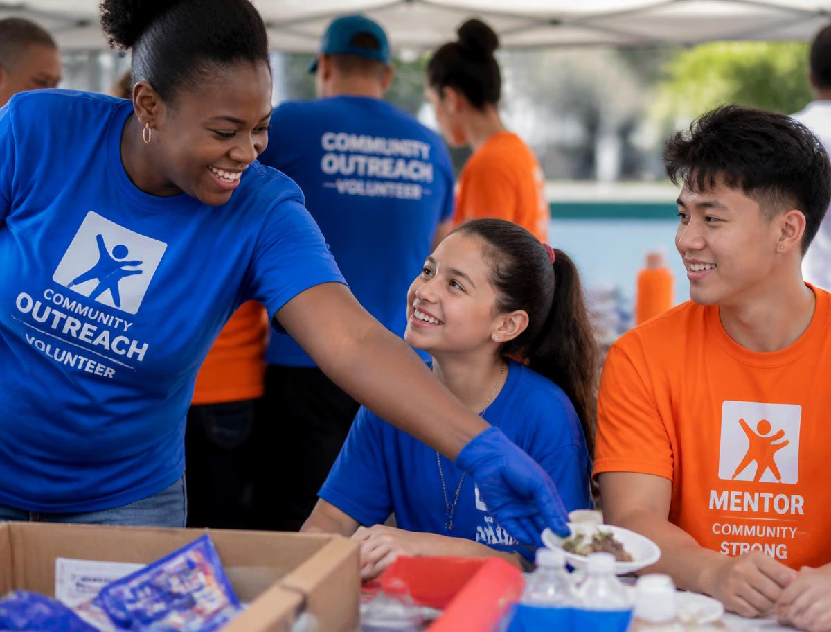 Community outreach volunteers in blue and orange shirts serving neighbors at an event